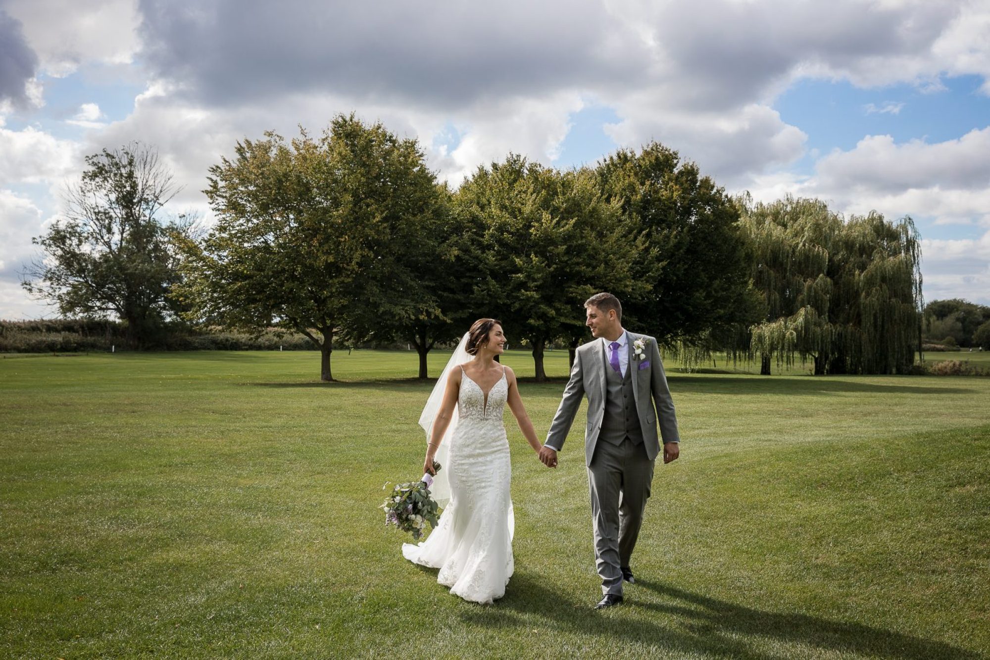 Bride and groom holding hands walking across a green landscape in Nottingham
